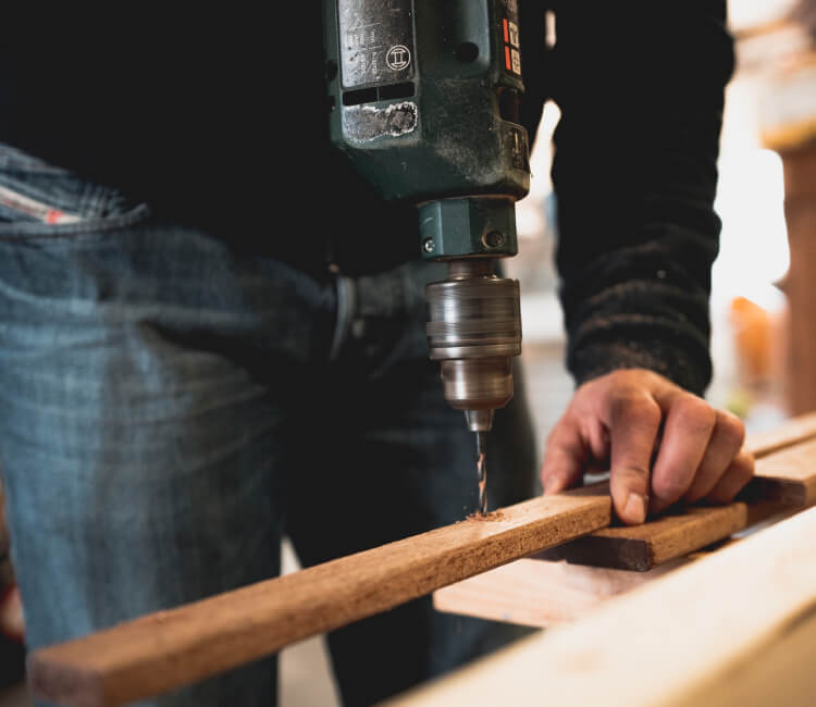 man drilling a hole in a plank of wood