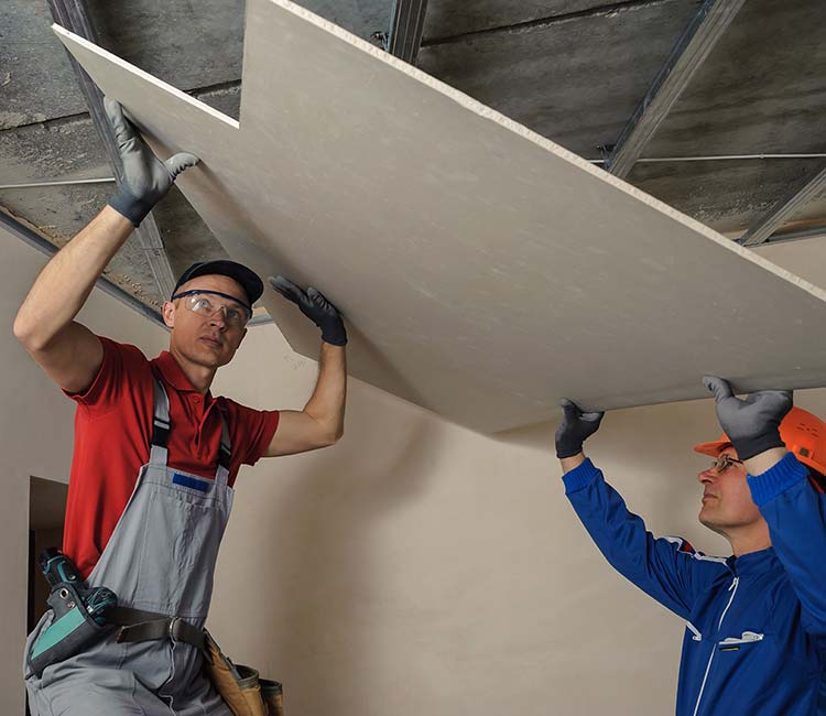 two men one in red and one in blue lifting a piece of drywall