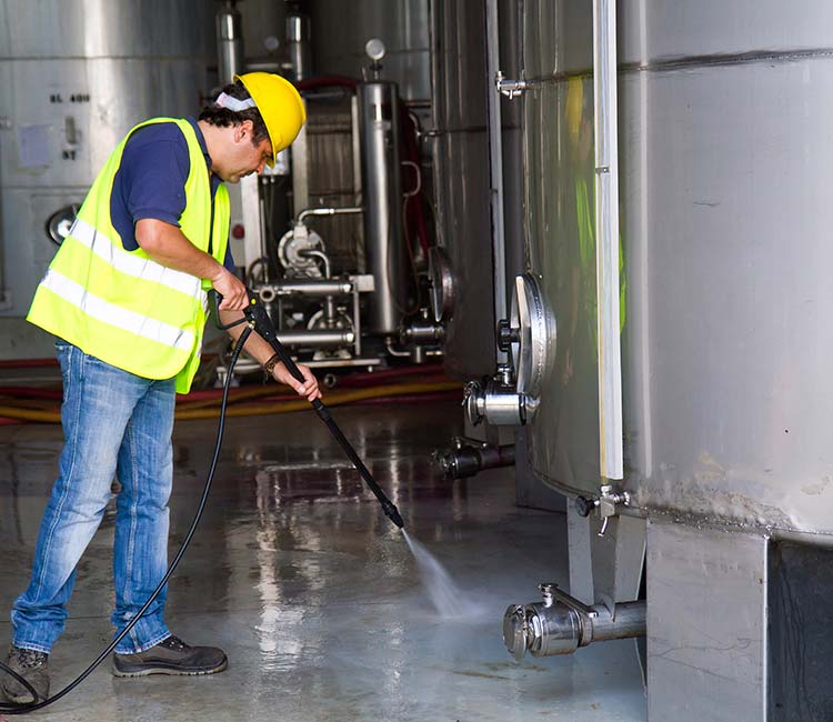 a man in a yellow traffic vest and hard hat pressure washing a floor